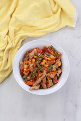 Meat with vegetables and sesame seeds on gray background with yellow cloth