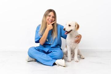 Young veterinarian woman with dog sitting on the floor happy and smiling