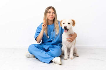 Young veterinarian woman with dog sitting on the floor with fingers crossing and wishing the best