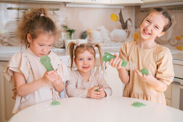 Three sisters playing slime on a kitchen, happy kids lifestyle.