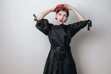 A fashionable beautiful girl in a black dress, straightens her red little hat with her hand. white background