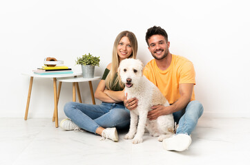 Young caucasian couple with dog staying at home keeping the arms crossed