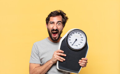young crazy bearded man dieting angry expression and holding a weight scale