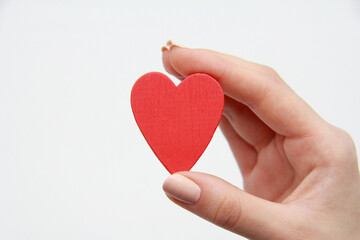 A woman's hand holds a red wooden heart on a white background.Health concept, love,organ donation, mindfulness,well-being, family, World Heart Day, Health Day, National Organ Donor Day.Copyspace