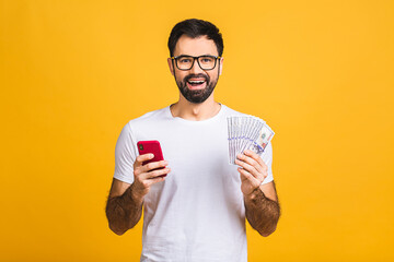 Happy winner! Excited young bearded man in casual holding lots of money in dollar currency and cell...