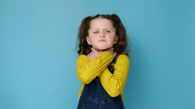 Unhealthy little girl child touch neck feels discomfort painful feelings hard to swallow, sore throat pain irritation or loss of voice, models over blue studio background. Tonsillitis angina concept