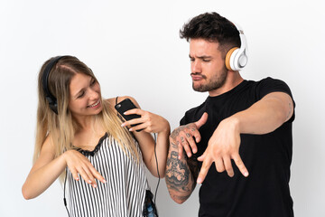 Young caucasian couple on white background listening music and dancing