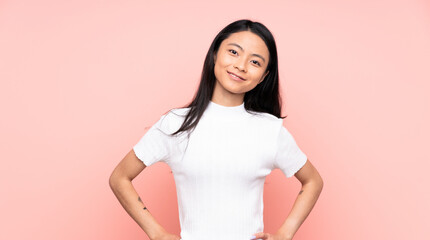 Fototapeta premium Teenager Chinese woman isolated on pink background posing with arms at hip and smiling