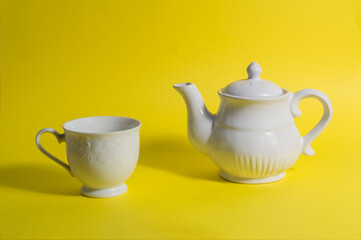 white ceramic teapot and cup, isolated on yellow background