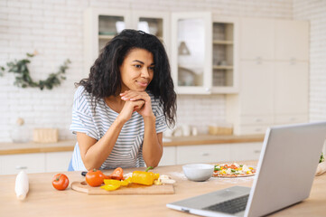 Interested mixed-race girl with hands on chin attentively watching cooking classes, learning how to...