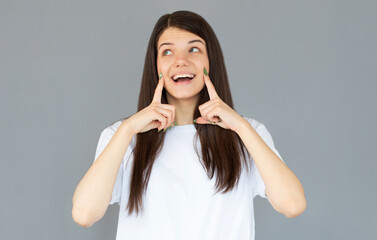 Enjoying her smooth skin. Beautiful young woman smiling while touching her cheeks and standing against grey background