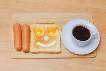 morning breakfast: two sausages, a toast with eggs in the form of a smiling face and a cup of coffee on a wooden board