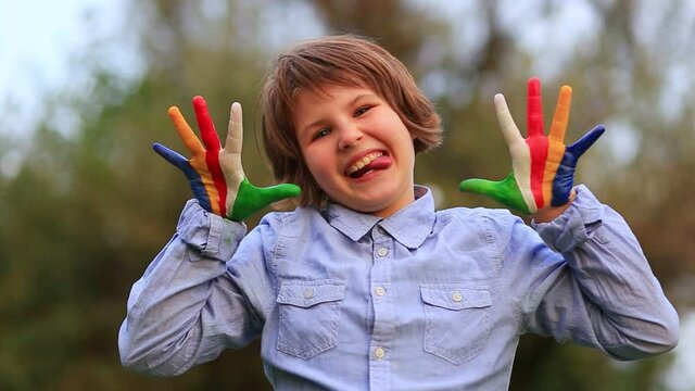 Kid play paint rainbow hands. Outdoor portrait of cheerful kid girl show hello gesture with hands painted in Seychelles flag colors. 