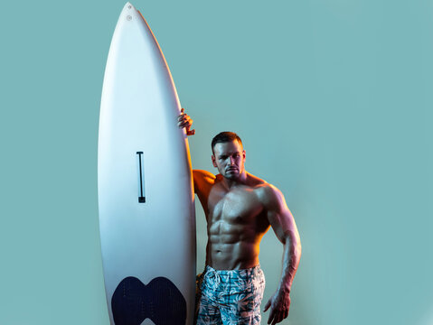 Serfer man with surfboard. Surfing hobby concept. Active lifestyle. Male beach leisure, summer vacation. Sexy muscular surfer with a surfboard. Summer boy, isolated on blue.