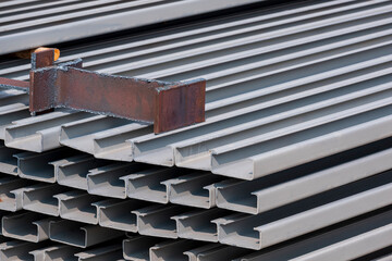 Steel beam piece on pile of gray rustproof C light lip channel steels in construction site area