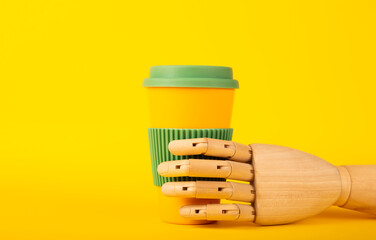 Fototapeta na wymiar Wooden mannequin hand holding reusable coffee cup on a yellow background with space for text