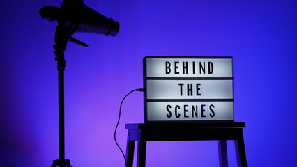 Behind the scenes letterboard text on Lightbox or Cinema Light box. Multi color LED on background. Sillhouette flash snoot hood on tripod. video production studio. Behind the scene Lightbox
