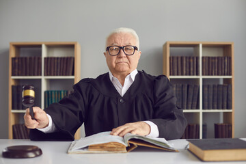 Portrait of a stern mature judge knocking with a hammer passing sentence and announcing that the...