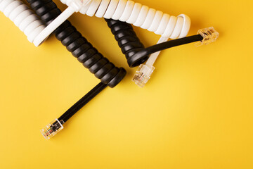 Compressed black and white spiral phone cord with connectors on yellow background.