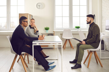 Interview, meeting, business negotiations concept. Group of young black and caucasian business partners discussing common project or interviewing young black man candidate in office interior