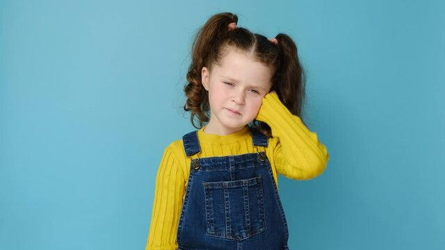 Frowning little preschool girl kid touch ear closed it with finger hurt suffers from earache strong pain, isolated on blue studio background, small child look at camera annoyed by loud noise concept