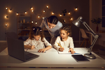 Family doing homework sitting at desk at home late in the evening. Children drawing pictures in...