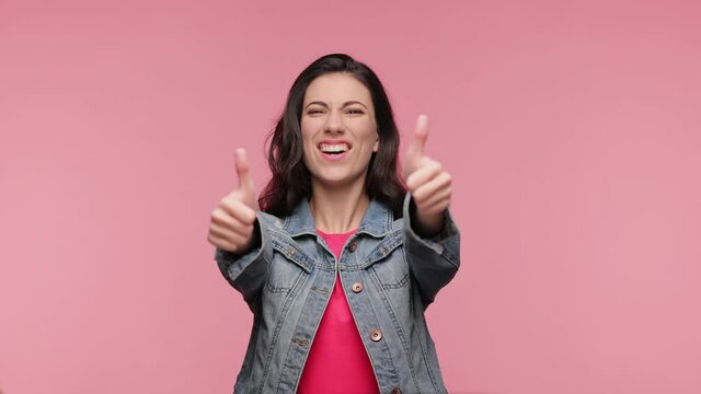 People lifestyle concept. Looking camera showing thumbs up. Cheerful joyful young Caucasian woman 20s years old in casual denim jacket pink t-shirt posing isolated on pink background in studio.