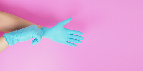 Obraz na płótnie Canvas Hand is pulling blue latex gloves on pink background.