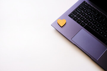 Metallic laptop on white table with tablet and wooden figure of yellow heart