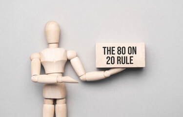 Wooden man shows with a hand to white board with text The 80 on 20 Rule,concept