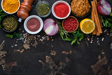 Set of Indian fragrant spices and herbs on a black stone background. Turmeric, dill, paprika, cinnamon, saffron, basil and rosemary in a spoon. Top view. Mock up.