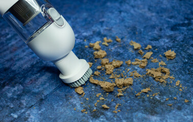 The white mini portable vacuum cleaner removes dirt. bread crumbs. on a blue background