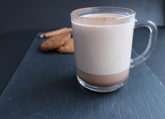 a cup of hot chocolate cocoa with biscuits in the background on a black background with a place for text and copyspace