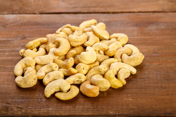 Cashew nuts are sprinkled on a dark wooden table.