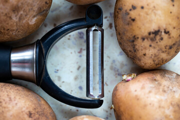 Several organic potatoes and a potato peeler on the table. Made in natural light, soft shadows.