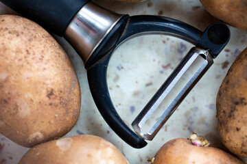 Several organic potatoes and a potato peeler on the table. Made in natural light, soft shadows.