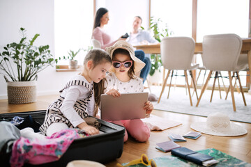 Small girls with tablet indoors at home, packing for summer holiday.