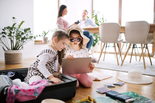 Small girls with tablet indoors at home, packing for summer holiday.