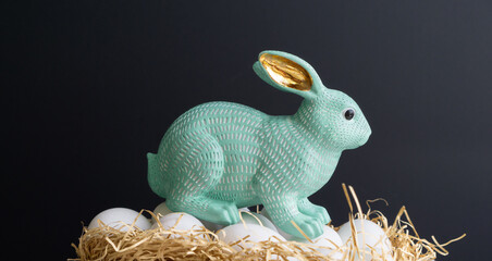 Figurine of turquoise rabbit, chicken eggs on a black background.