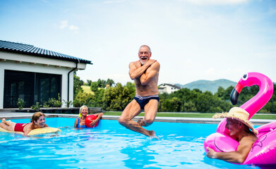 Group of cheerful seniors in swimming pool outdoors in backyard, jumping.
