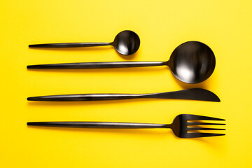 Dark cutlery on yellow background. Black kitchen utensils set. Top view. Bright and stylish kitchen mood