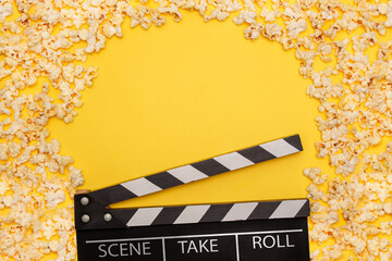 Black and white movie clapperboard on yellow background with freshly popped popcorn surrounding the...