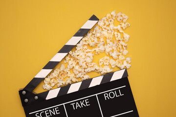 Movie and TV clapperboard on yellow background with freshly popped popcorn in center