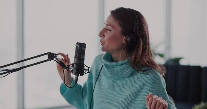 Cool excited young woman singing song into micrphone headset recording audiotrack inside home. Hobby activity. Talented people. Music performance.
