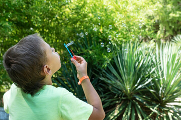 White caucasian boy is blowing soap bubbles in green summer park. Summer vacation activities Happy childhood.