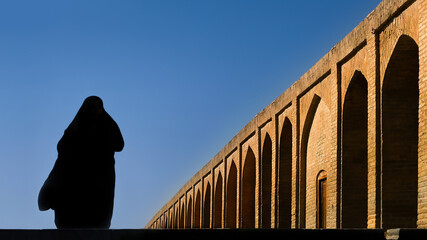 Silhouette of a Persian woman in national dress on the old Khaju (Pol-e Khaju) bridge in Isfahan. Iran. Ancient Persia.