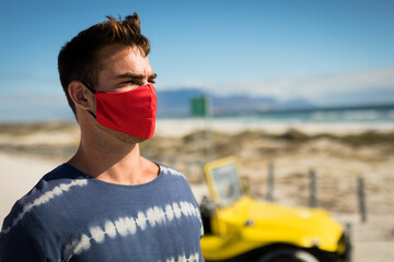 Happy caucasian man wearing face mask next to beach buggy looking toward sea