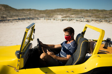 Caucasian man wearing face mask sitting in beach buggy using smartphone