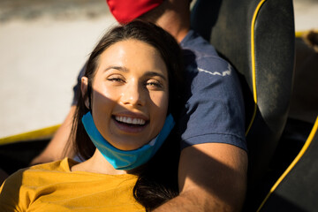 Happy caucasian couple wearing face masks sitting in beach buggy smiling