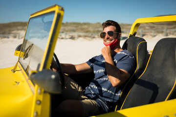 Caucasian man wearing face mask sitting in beach buggy smiling